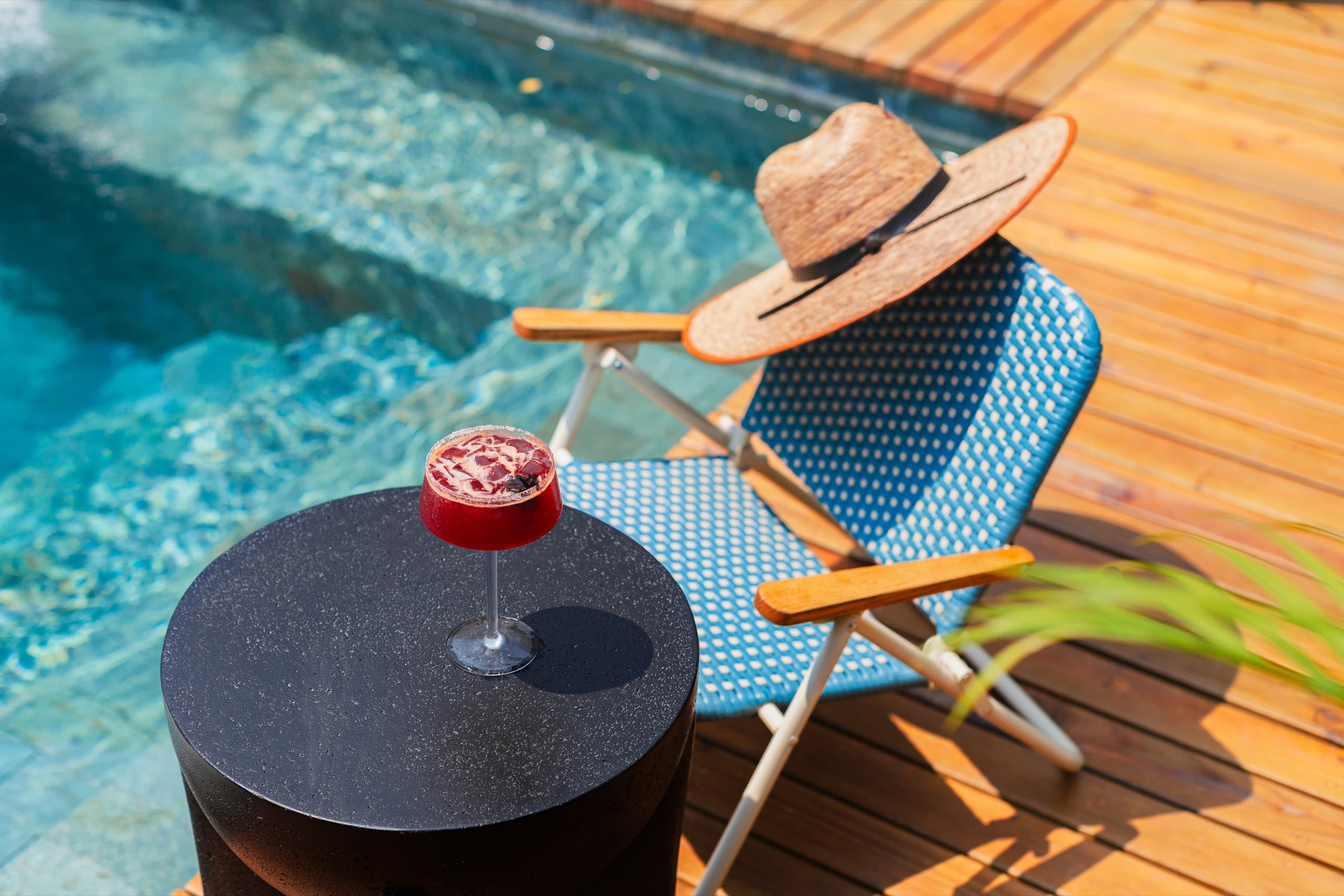Tumbona junto a la piscina con un sombrero y un cóctel